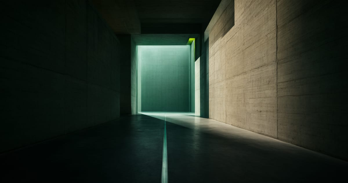 Corredor longo de concreto entre duas estruturas à noite, com um limiar iluminado ao fundo.